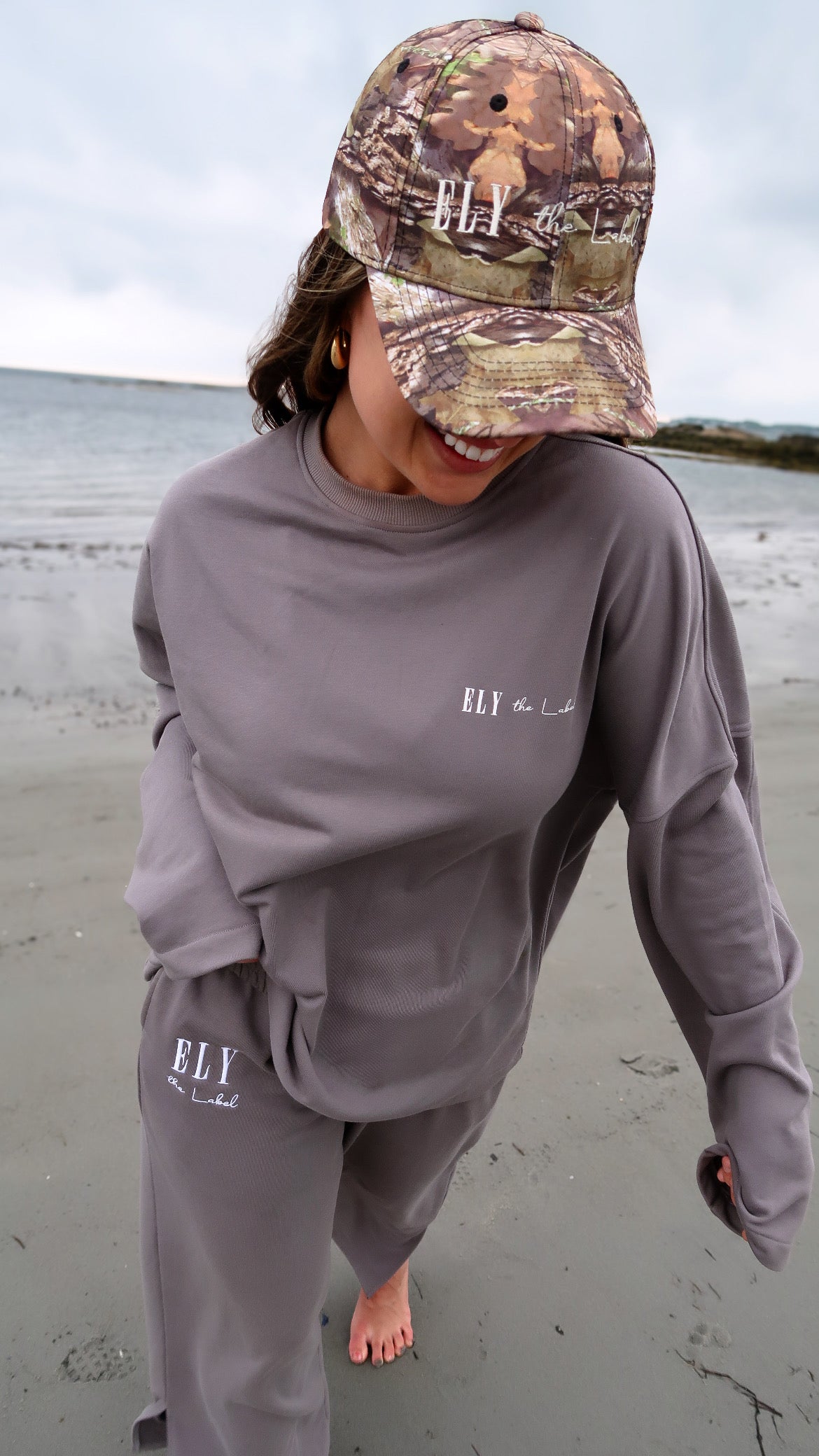 Women and menโs camouflage hat ELY the Label in womenโs loungewear on beach on model Eileen Hayman
