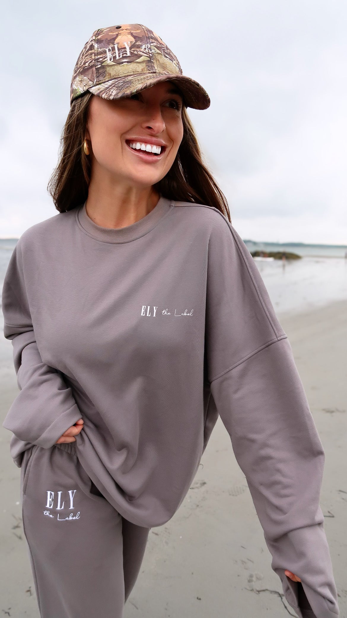 Women and menโs camouflage hat ELY the Label in womenโs loungewear on beach on model Eileen Hayman
