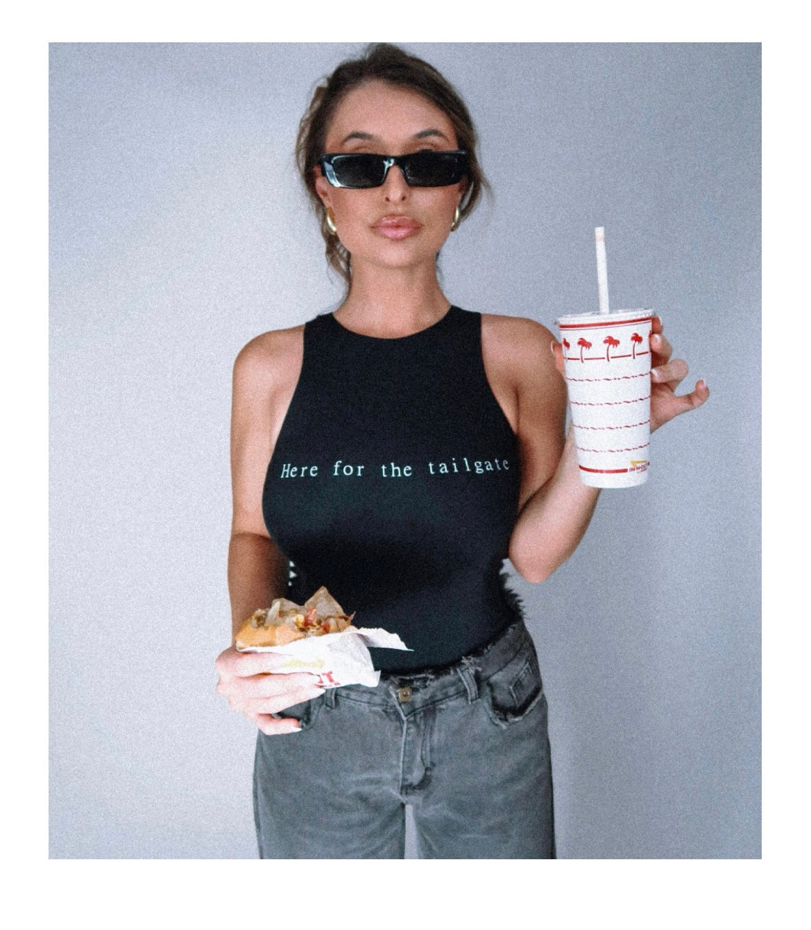 Model Eileen Hayman wearing Here for the tailgate high neck bodysuit in espresso, showcasing a sleek-form fitting design with flattering high neckline. Paired with distressed denim for a sporty, chic look, perfect for game day. Eating In-n-Out burger