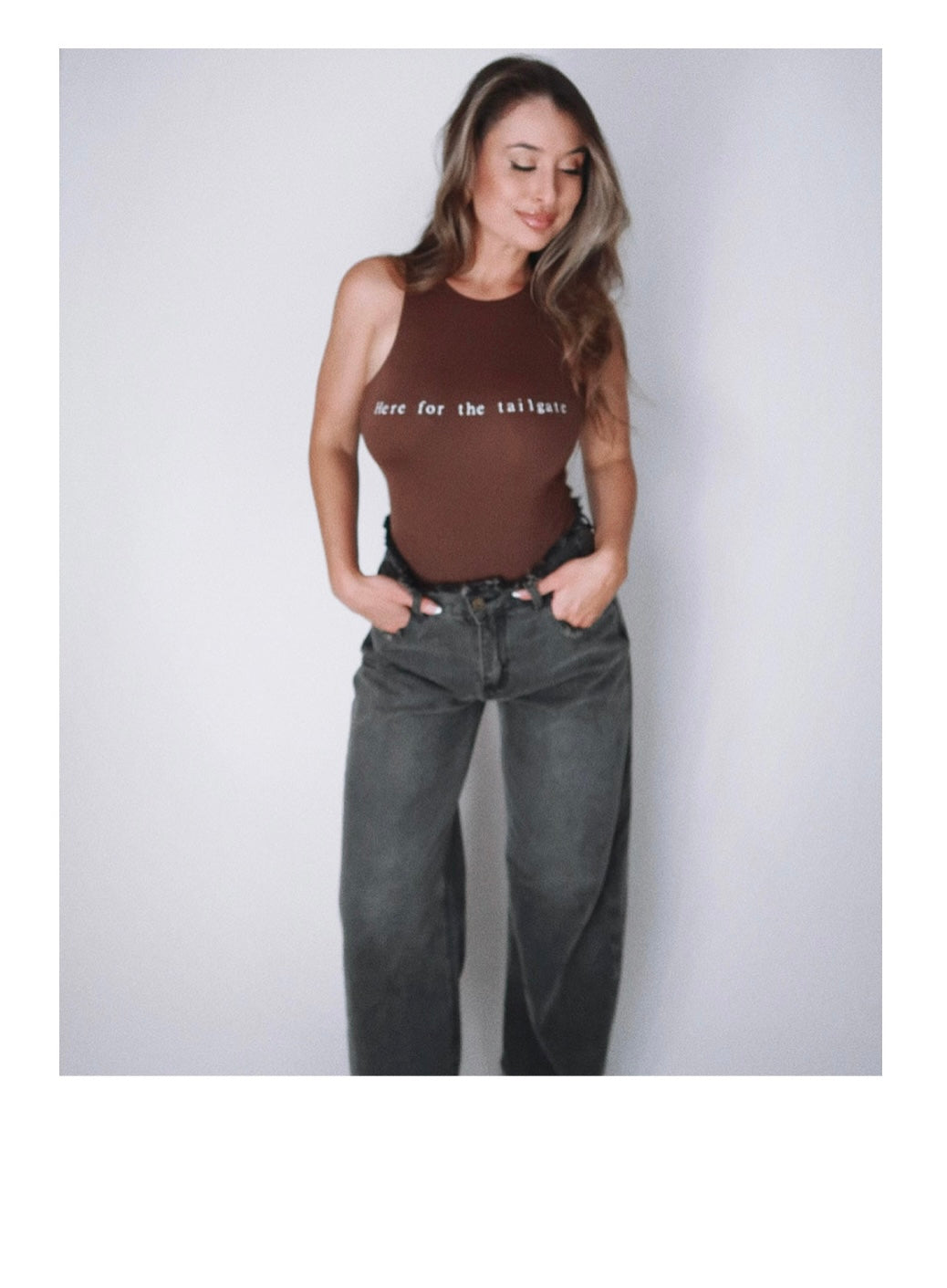 Model Eileen Hayman wearing Here for the tailgate high neck bodysuit in espresso, showcasing a sleek-form fitting design with flattering high neckline. Paired with distressed denim for a sporty, chic look, perfect for game day.