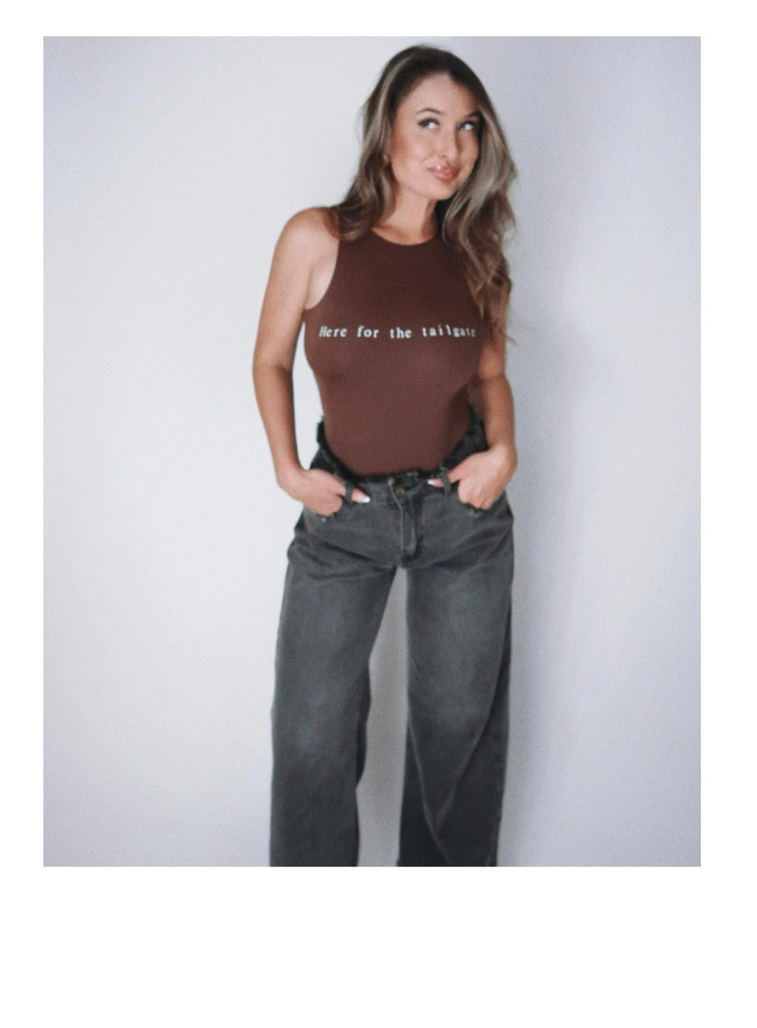 Model Eileen Hayman wearing Here for the tailgate high neck bodysuit in espresso, showcasing a sleek-form fitting design with flattering high neckline. Paired with distressed denim for a sporty, chic look, perfect for game day.